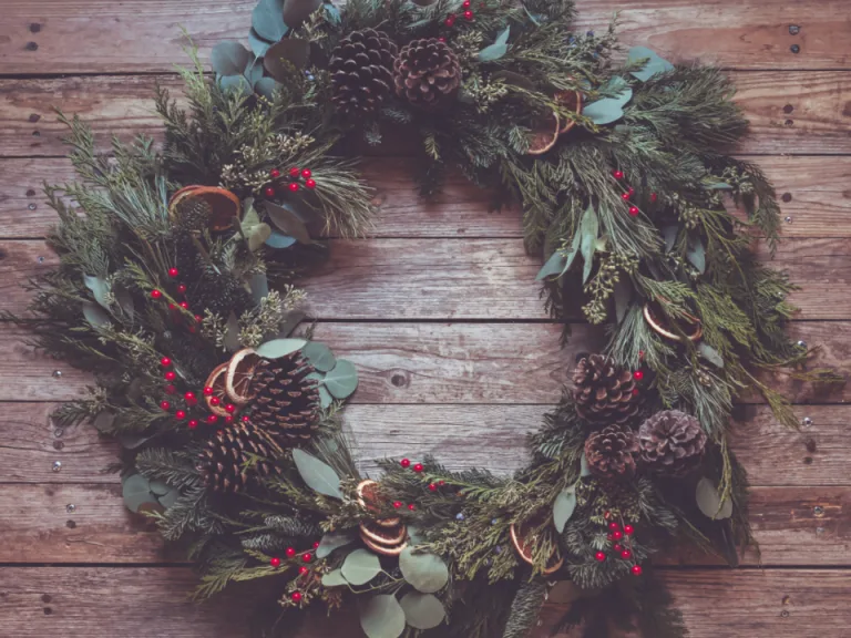Handmade evergreen holiday wreath with pine cones on a rustic wood background