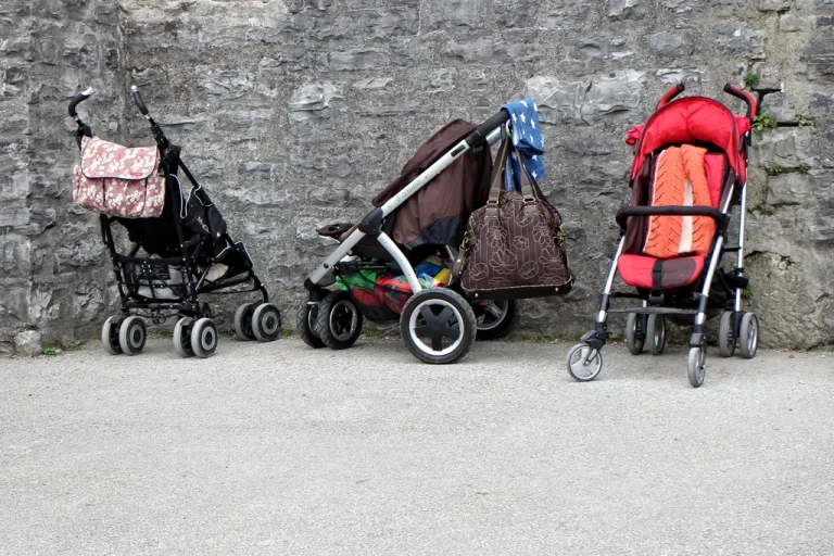 Three baby strollers parked against a stone wall