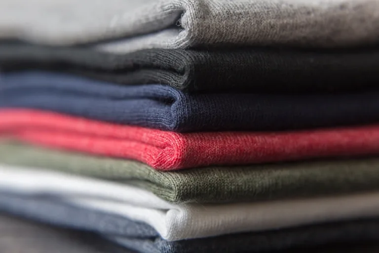 Stack of folded blank T-shirts in gray, black, navy, red, green and white
