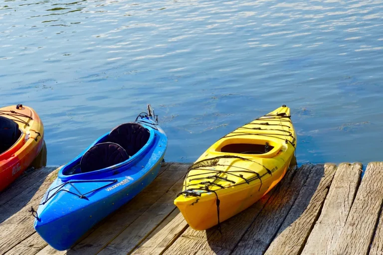 Red, blue and yellow sit-in kayaks resting on a wooden dock beside calm water