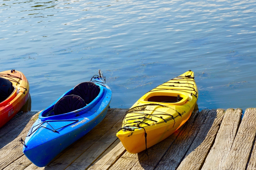 Red, blue and yellow sit-in kayaks resting on a wooden dock beside calm water