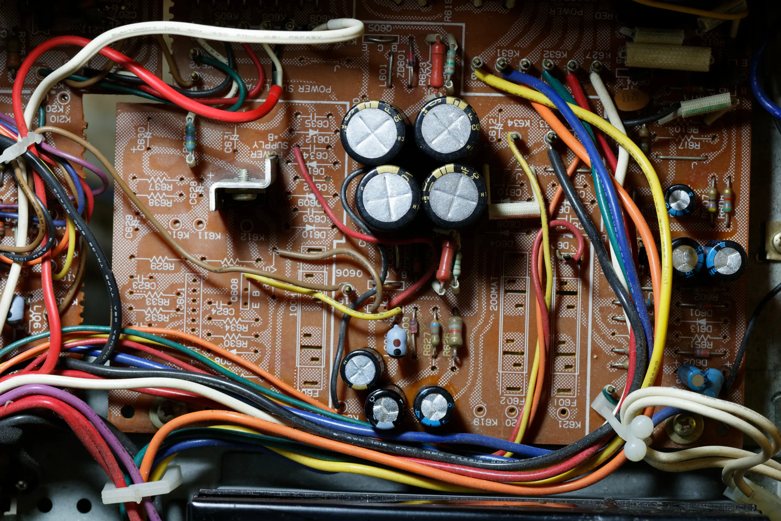 Inside an electronics unit showing a circuit board with replacement capacitors and colored wiring
