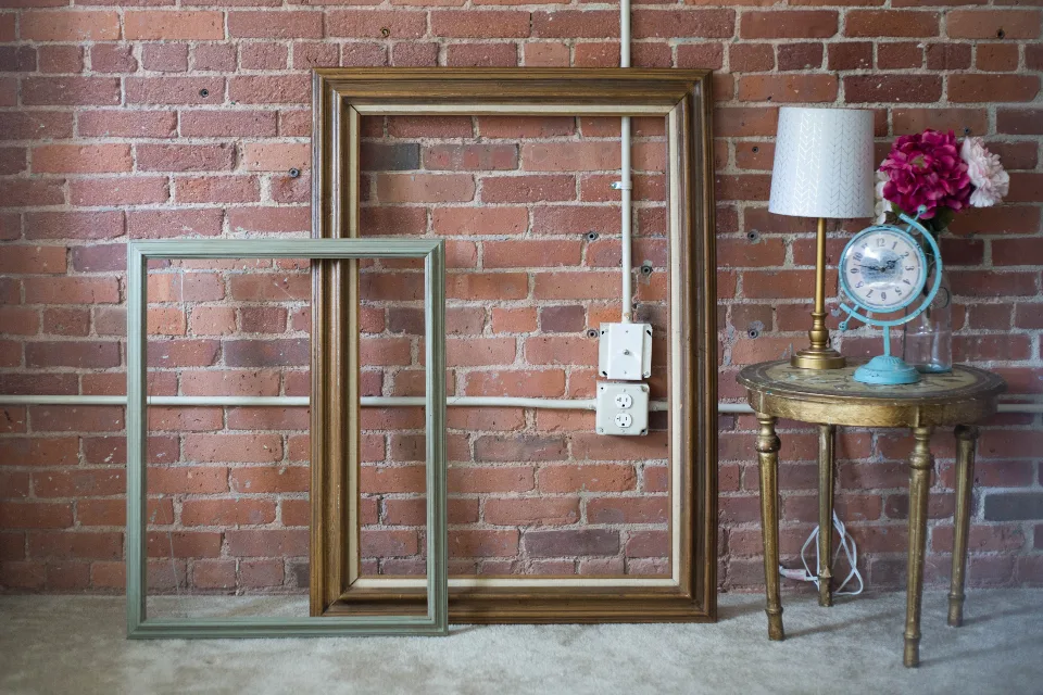 Empty wooden picture frames leaning against a brick wall beside a small side table