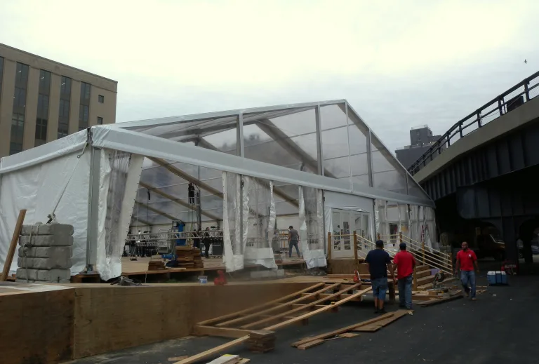 Crew assembling a large white frame event tent outdoors