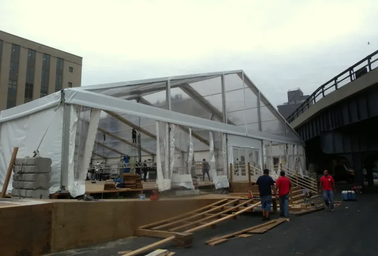 Crew assembling a large white frame event tent outdoors