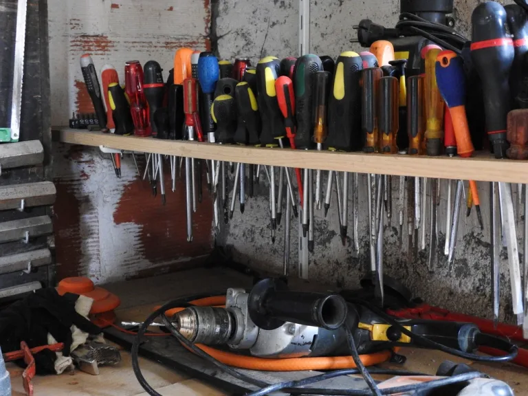 Rows of screwdrivers on a wooden shelf above a power drill in a home garage workshop