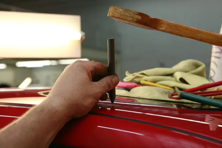 Hand working on the glossy red body panel of a car