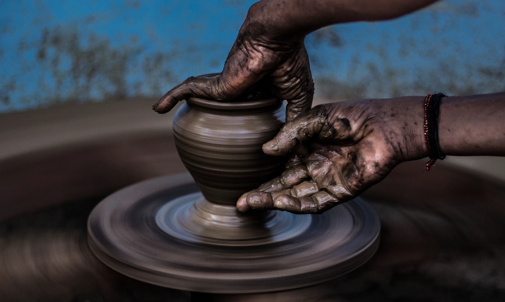 Clay-covered hands shaping a pot on a spinning pottery wheel