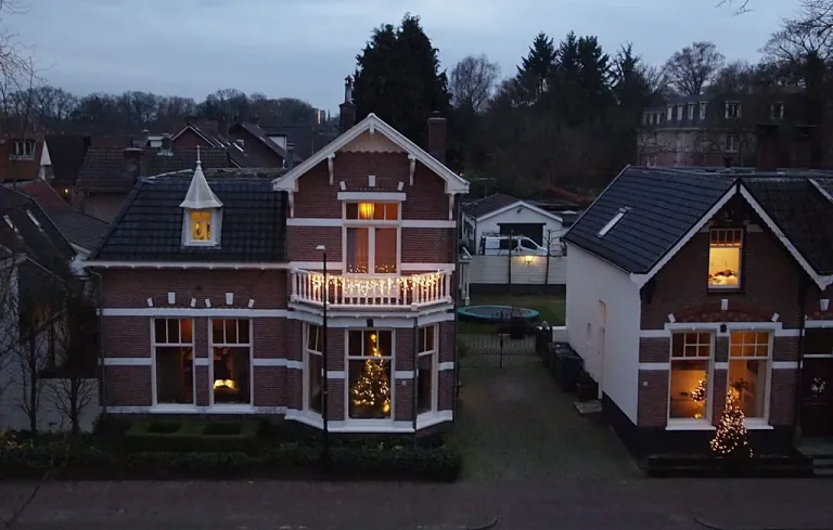 Brick houses at dusk decorated with holiday lights and lit Christmas trees