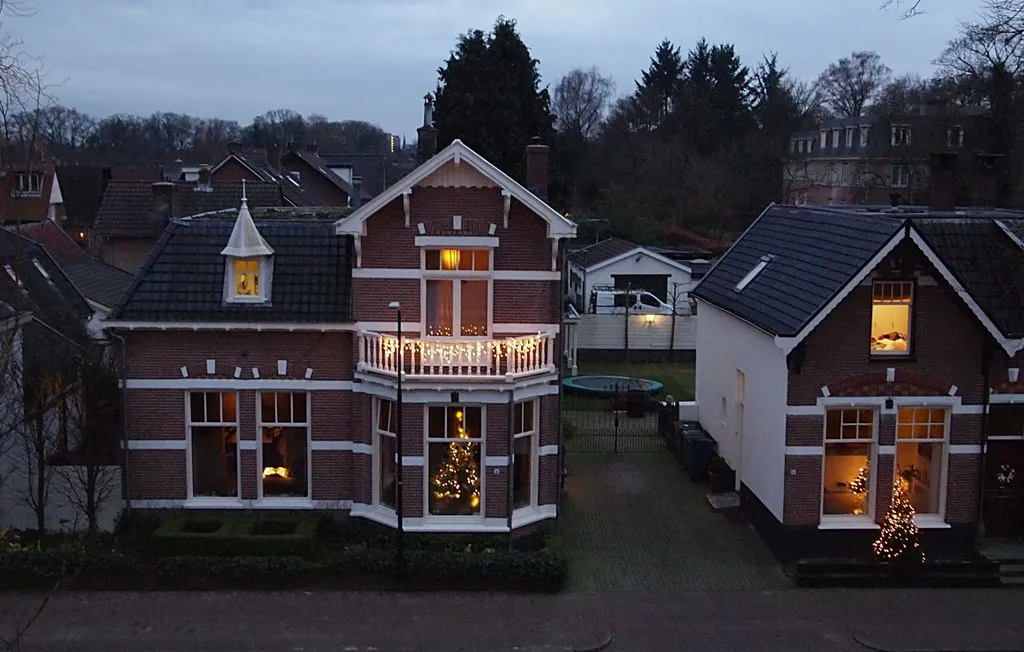 Brick houses at dusk decorated with holiday lights and lit Christmas trees