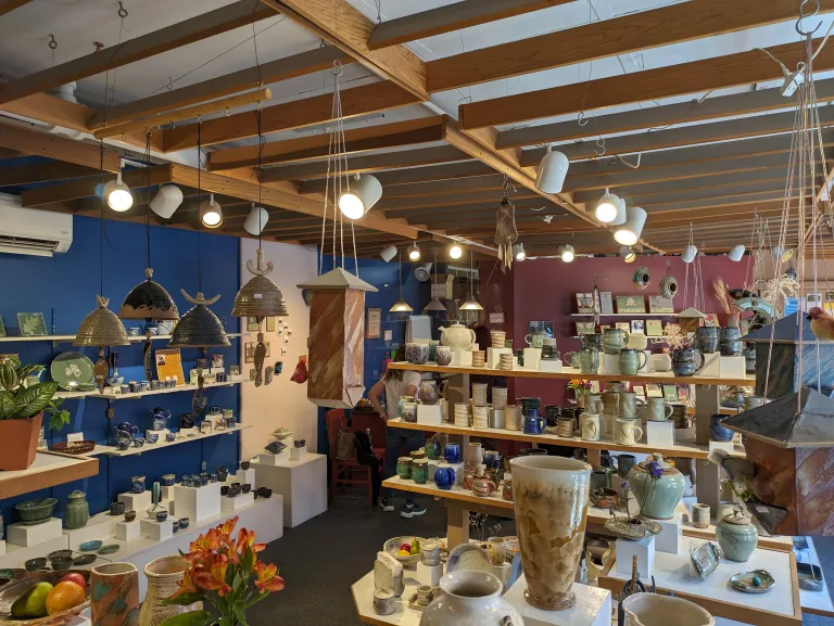 Small independent gift shop with shelves of handmade pottery mugs, vases and hanging lamps