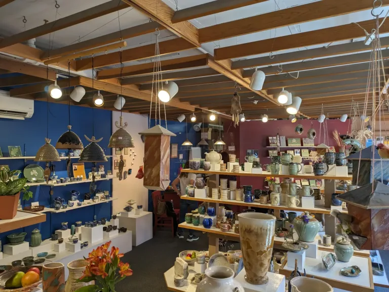 Small independent gift shop with shelves of handmade pottery mugs, vases and hanging lamps