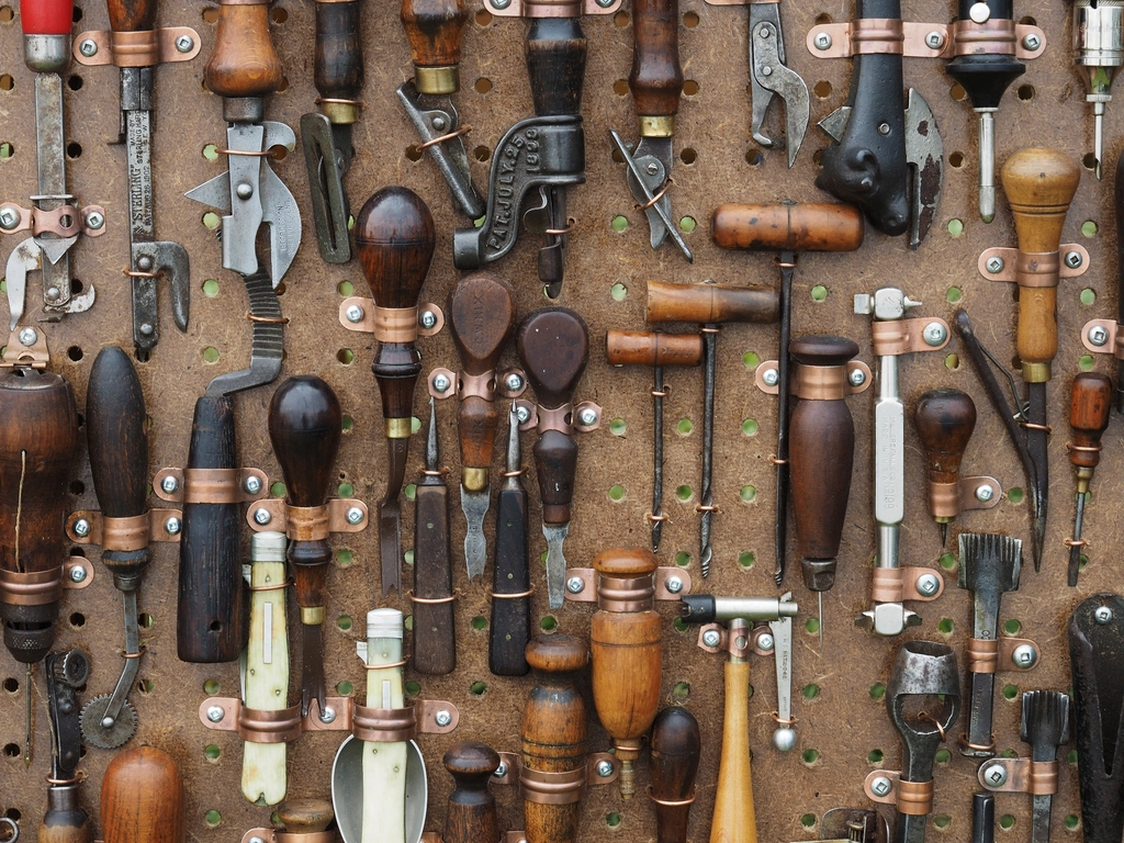 Rows of wooden-handled hand tools hanging on a workshop pegboard
