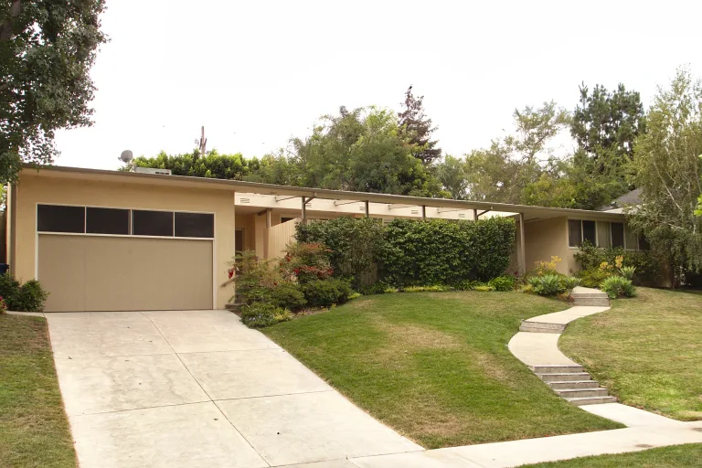 Mid-century single-story house with an attached garage and sloping driveway on a residential street in Los Angeles