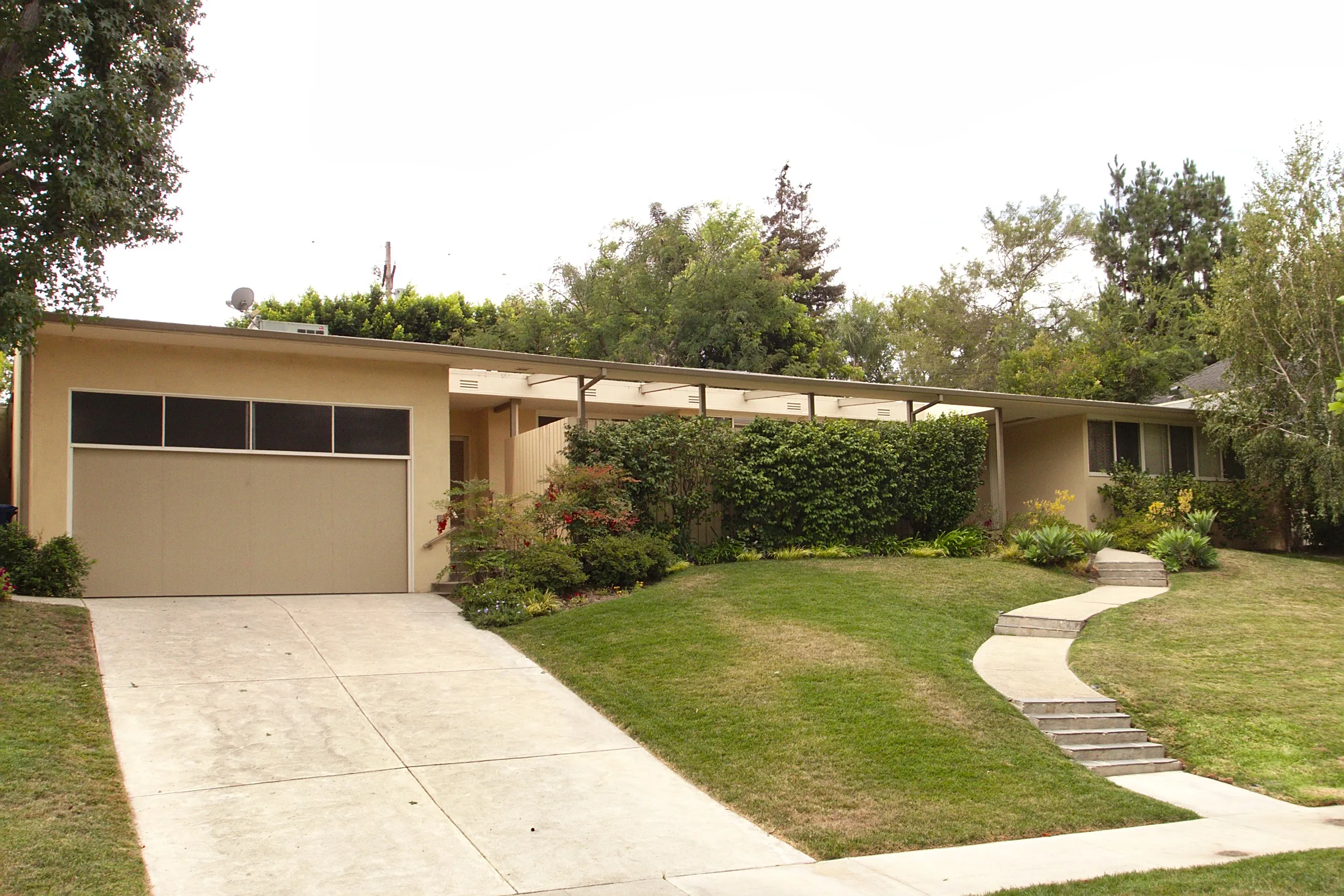 Mid-century single-story house with an attached garage and sloping driveway on a residential street in Los Angeles