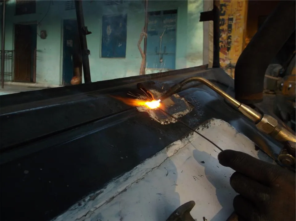 Gloved hands using a torch to work on a metal piece in a dim workshop