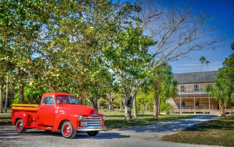 Red pickup truck with a wooden bed parked on a tree-lined drive