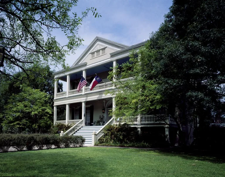 Two-story white house with wide porches and flags in San Antonio’s historic King William District