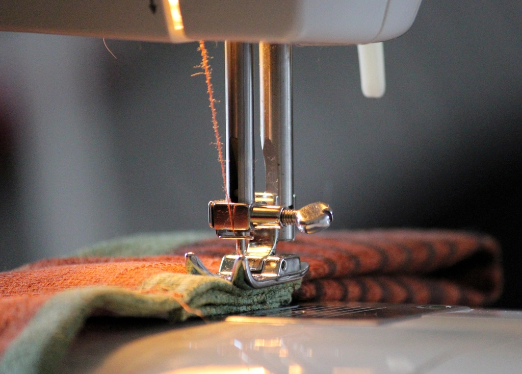 Close-up of a sewing machine presser foot stitching heavy striped fabric