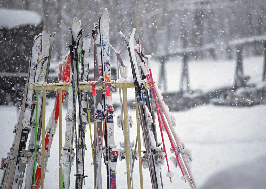 Skis and poles standing in a rack in falling snow