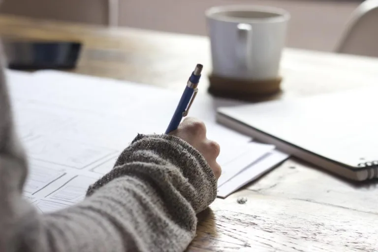 Hand writing notes with a pen at a wooden table