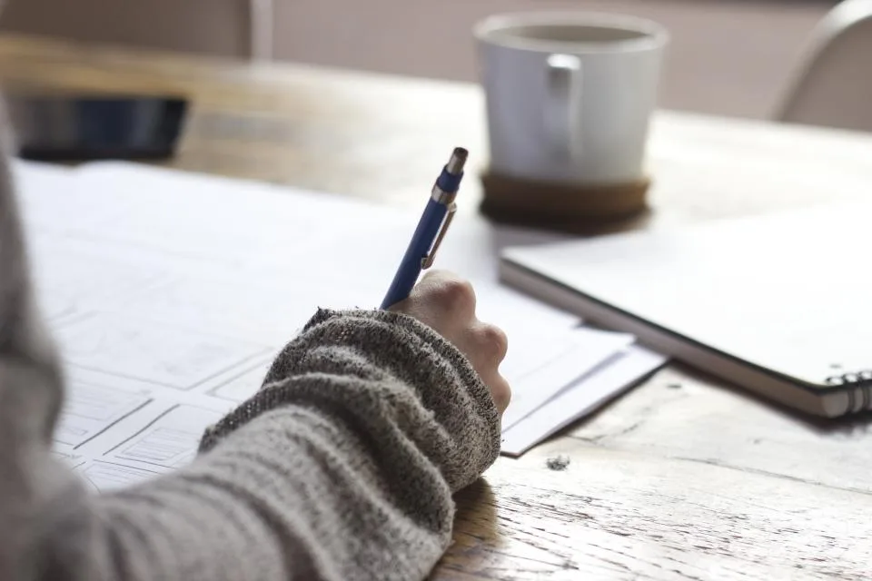 Hand writing notes with a pen at a wooden table